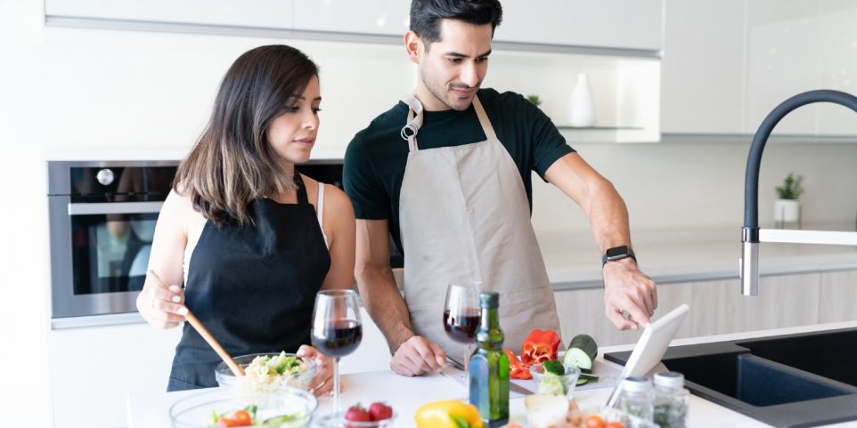 Latin young couple watching recipe on internet and preparing food at home