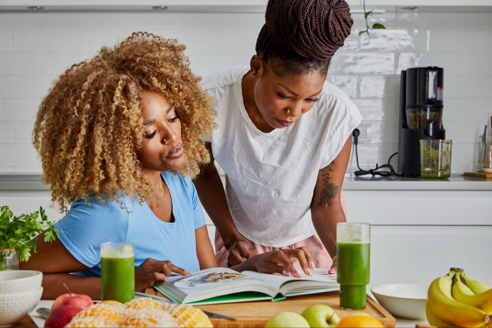 A beautiful black young adult woman in the kitchen, fresh vegan or vegetarian food preparation at the kitchen table, representing healthy lifestyle, an image with a copy space